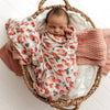Newborn baby wrapped in a strawberry-patterned blanket in a wicker basket.