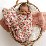 Newborn baby wrapped in a strawberry-patterned blanket in a wicker basket.