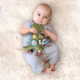Baby holding a green dinosaur toy on a white fluffy surface