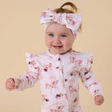 Baby wearing a floral outfit and headband on a beige background