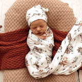 Newborn baby wrapped in a floral swaddle with a matching hat, lying on a textured surface.