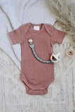 Brown baby onesie with a teething toy on a textured surface