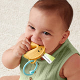 Baby chewing on a yellow teething toy with a smiley face, wearing a green outfit.