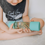 Child holding a teal bottle with a clear liquid and small objects inside, wearing a black 'Good Vibes' shirt.
