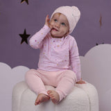 Baby in pink outfit sitting on a cloud-like surface with a purple starry background
