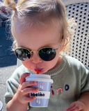 Child wearing sunglasses drinking from a bbeeino cup outdoors.