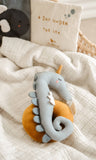 Plush toy dragon on an orange ball with a soft blanket and pillow in the background
