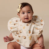 A baby wearing a cream-colored bib with a printed pattern of bumblebees and small flowers, styled with a matching yellow bow in her hair, set against a solid beige background.