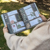 Person holding a book with botanical illustrations outdoors