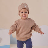 Baby wearing a brown sweater and knit hat on a neutral background