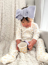 Child wearing a large blue bow sitting on a couch with a cup.