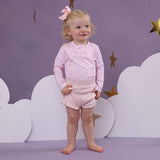 Young child in pink outfit standing against a purple background with cloud and star decorations