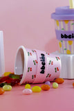 Pink cup with cherry design and 'bbeino' branding on a pink background with jelly beans.