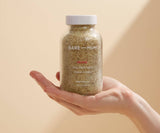 Hand holding a jar of Bare Mum bath salts against a beige background