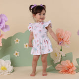 Young girl in a floral dress standing among large flowers on a beige background
