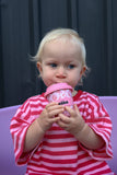 Child in a red and white striped outfit holding a pink cup with a dark curtain background