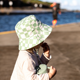 Person wearing a green checkered hat on a beach with water and sky in the background