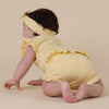 Baby in a yellow outfit with ruffles on a beige background