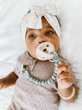 Baby wearing a headband and holding a teething ring with a pacifier