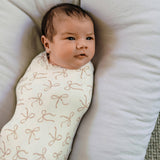 Newborn baby wrapped in a swaddle with bow pattern on a soft surface