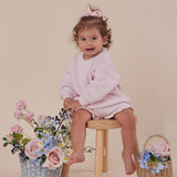 Child in pink outfit sitting on a stool with flowers and a basket on a beige background