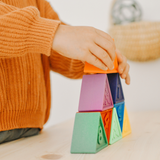 Child's hand stacking colorful geometric blocks on a light surface.