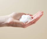 Hand holding a small ball of white snow against a beige background