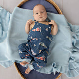 Baby in a blue romper with car pattern lying on a blue blanket in a basket.