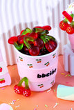 Cup filled with gummy worms on a colorful surface with 'bbcinco' branding.