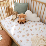 A fitted crib sheet with a cute cow and calf pattern is shown in a wooden crib, styled with plush toys and pillows.