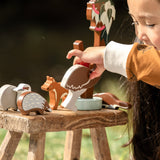 Child playing with wooden animal toys on a wooden stool outdoors.
