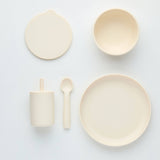 Set of beige ceramic plates, bowls, and utensils on a light gray background