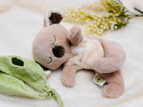 Plush toy elephant lying on a soft surface with a green leafy item nearby