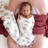 Newborn baby wrapped in a floral blanket with a pink headband, lying on a pink pillow.