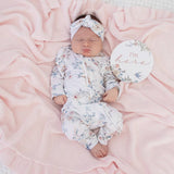 Newborn baby in floral outfit with 'I'm here' sign on pink blanket