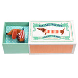 Miniature sausage dog toy in a box with a decorative label on a white background