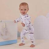 Baby in a white outfit with boat pattern standing next to a gift bag with an anchor design.