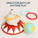 A baby toy set featuring a white seal sitting on a red and white circus-style base, with a yellow ring around its neck, a blue and yellow ball with a yellow star, and two plastic rings in light blue and red. Text at the top reads 'GREAT FOR BATH OR ANYTIME PLAY'.