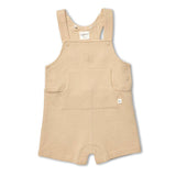 A light beige corduroy baby overall romper with adjustable shoulder straps, a front patch pocket, and a small embroidered monogram on the chest, shown on a plain white background.