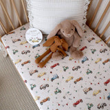 Crib with patterned sheet, stuffed animals, and a round sticker on a neutral background