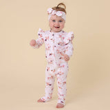 Baby wearing a floral onesie and headband on a beige background