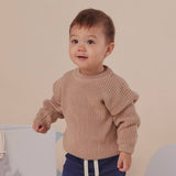 Child wearing a beige sweater against a plain background