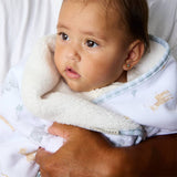 Baby wrapped in a white blanket with a pattern, held by an adult.