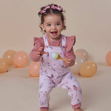 Child in pink outfit with floral pattern holding a toy, surrounded by balloons on a beige background