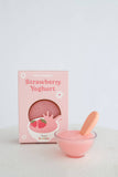 Pink strawberry yogurt with a spoon and packaging on a light gray background