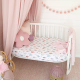 Children's crib with floral bedding, pink canopy, and decorative pillows in a nursery setting.
