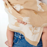 Beige and white patterned blanket being held by a child wearing blue jeans.