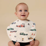 Baby wearing a bib with race car pattern on a beige background