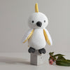 White and yellow stuffed toy on a wooden block with a minimal background