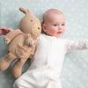 Baby holding a knitted teddy bear against a light blue background with subtle patterns